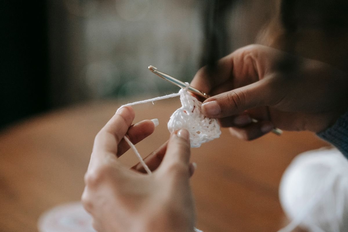 Hands working crochet fabric with a hook and light-colored yarn.