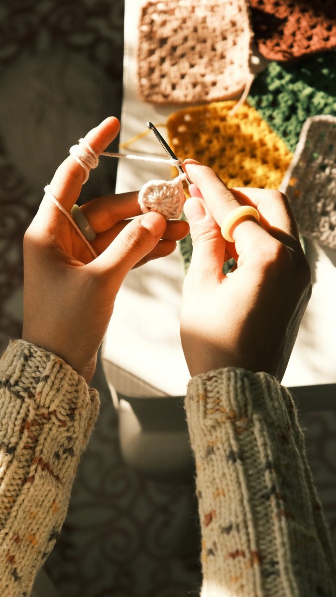 Hands crocheting colorful granny-square work in warm light.
