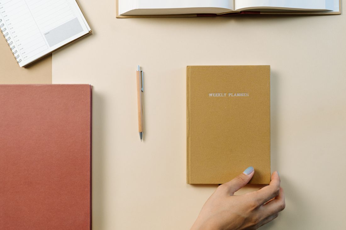 A weekly planner, notebook and pen on a desk.