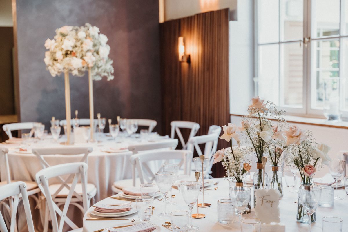 Luxurious wedding setup featuring white tablecloths, floral centerpieces, and elegant tableware in a bright venue.