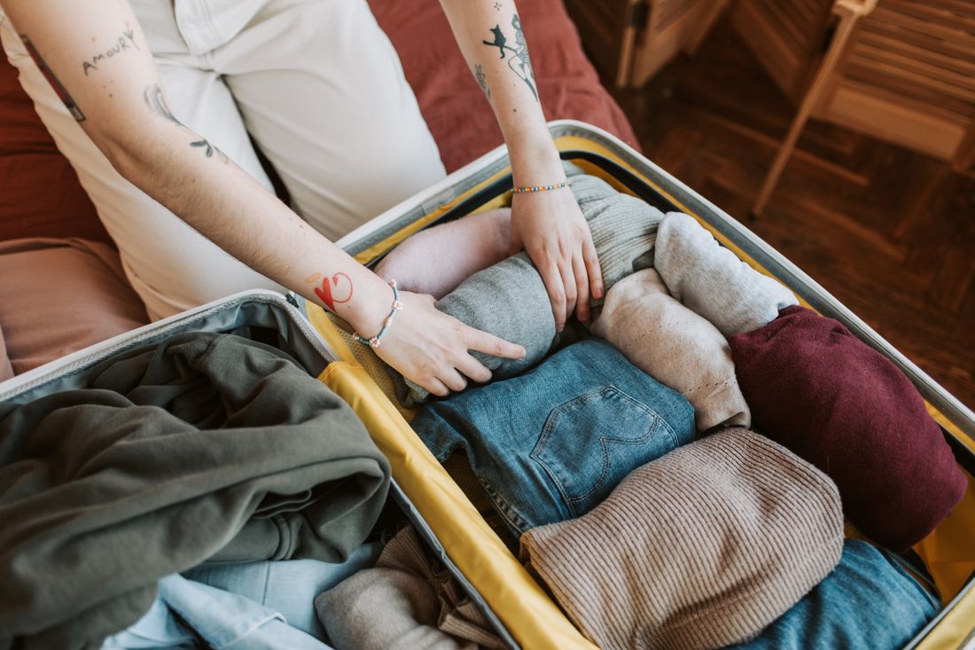 Hands packing clothing into a suitcase.